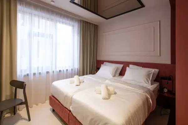 Kvarnersolutions hotel szoba, fehér ágynemű, piros ágyfej, napfényes ablak.